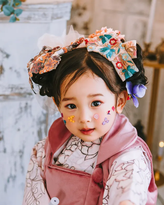 編み込みのお団子に刺繍のリボンを合わせた、被布の3歳の女の子