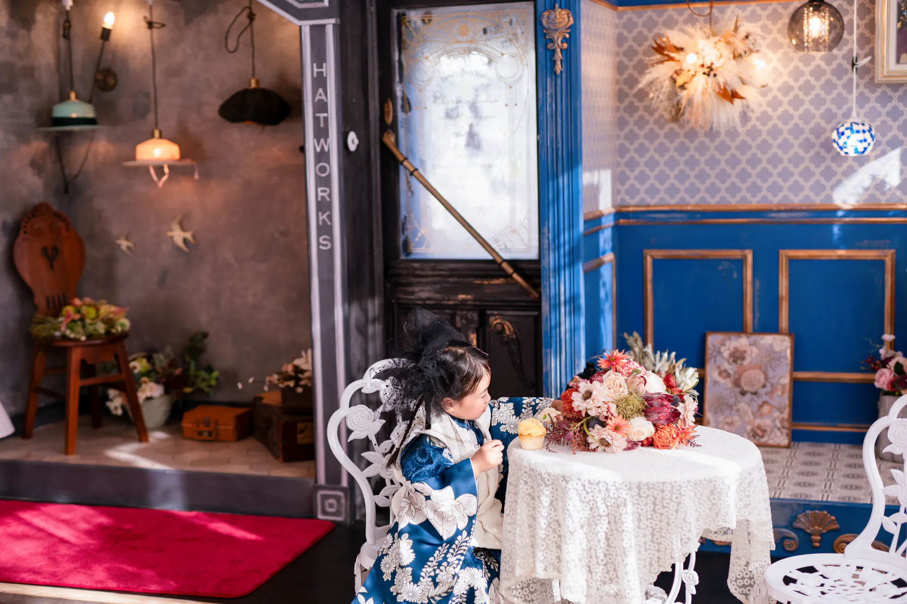 帽子屋と青いブティックの間で花を見つめる、青い着物の子ども