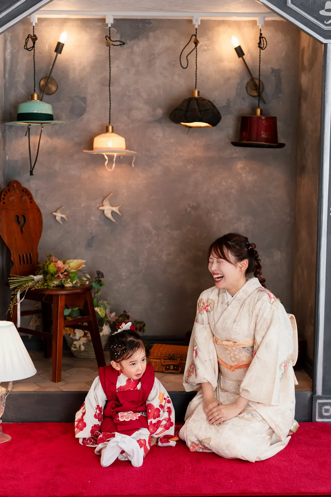 帽子屋の赤いじゅうたんで並んで座る、着物のお母さんと女の子