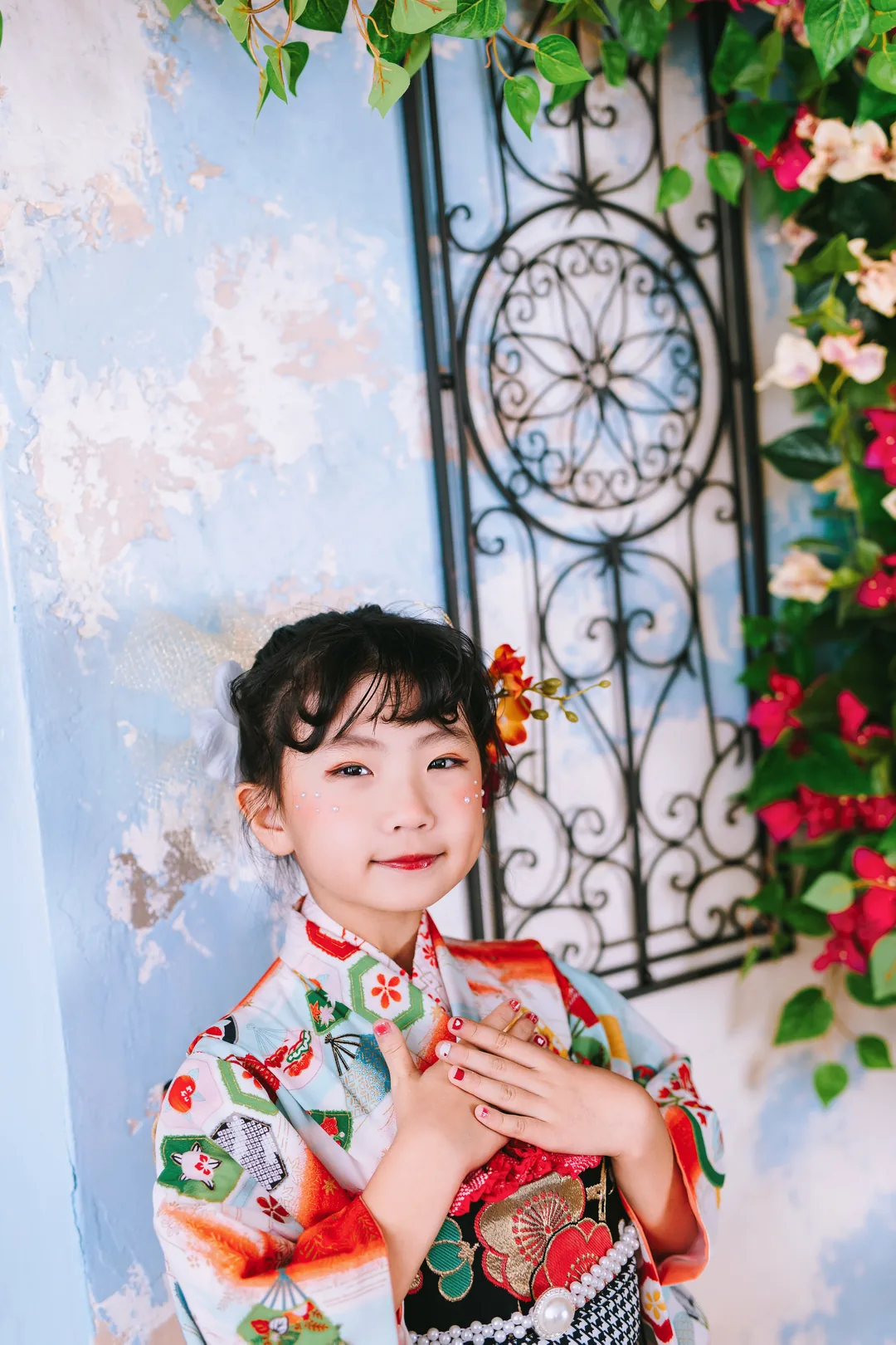 バラの窓辺で手を合わせてほほえむ、白地に扇の着物の女の子