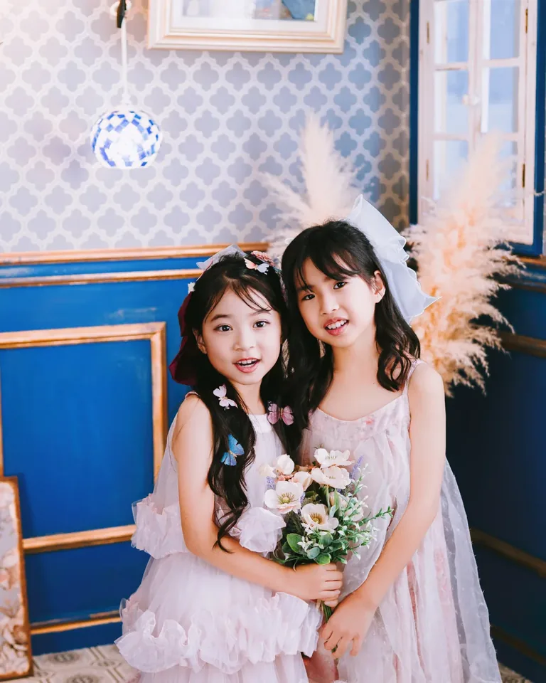 青いブティックで花束を持つ、洋装の子どもふたり